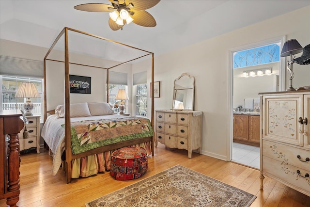 bedroom featuring ensuite bathroom, ceiling fan, light wood-style flooring, and baseboards