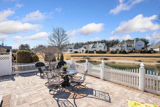 view of patio with a water view, a residential view, fence, and outdoor dining area