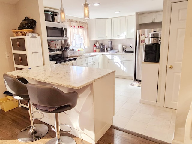 kitchen featuring appliances with stainless steel finishes, a breakfast bar area, hanging light fixtures, light stone countertops, and white cabinetry