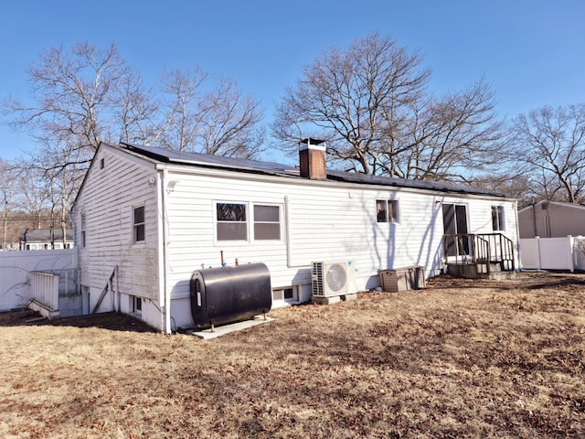 rear view of property with solar panels, fence, heating fuel, ac unit, and a chimney