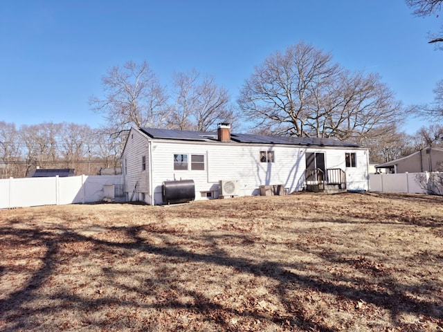 back of house featuring entry steps, a fenced backyard, roof mounted solar panels, a chimney, and heating fuel