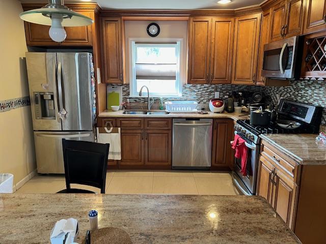 kitchen featuring light tile patterned floors, a sink, appliances with stainless steel finishes, decorative backsplash, and brown cabinetry