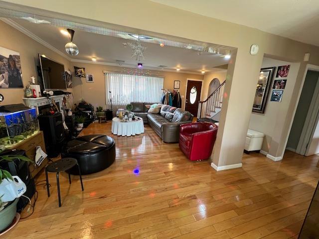 living room with stairs, baseboards, wood finished floors, and crown molding