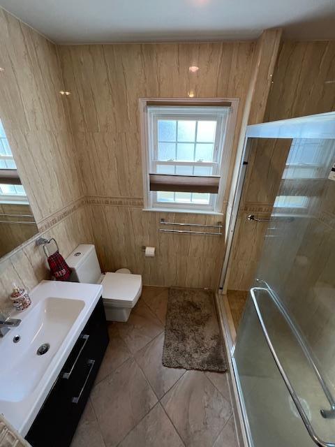 bathroom with tile walls, a shower stall, toilet, and vanity