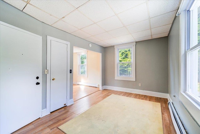 empty room with a baseboard heating unit, baseboard heating, light wood-type flooring, and a paneled ceiling