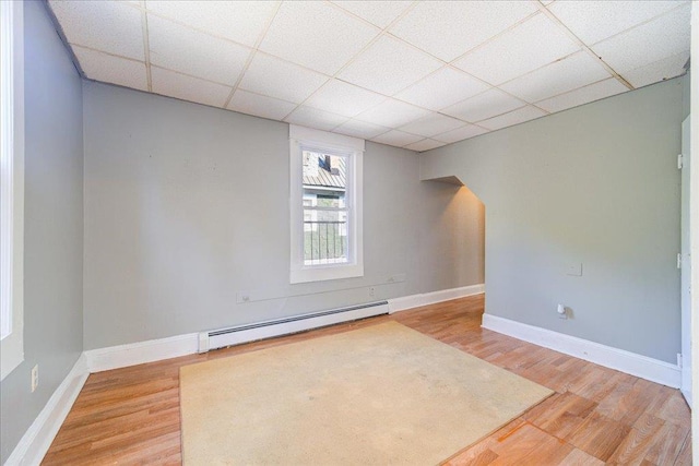 unfurnished room with a baseboard heating unit, a paneled ceiling, baseboards, and light wood finished floors