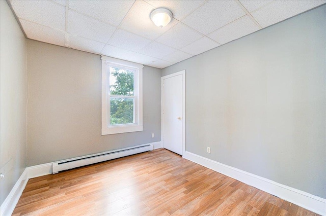 spare room featuring baseboards, a drop ceiling, light wood finished floors, and baseboard heating