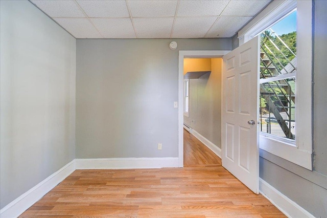 empty room with a paneled ceiling, light wood-type flooring, and baseboards