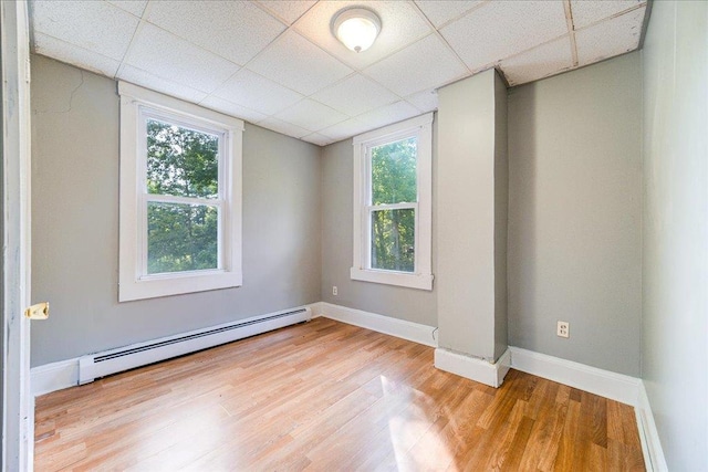 spare room featuring a baseboard heating unit, light wood-style flooring, a paneled ceiling, and baseboards