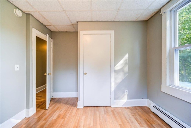 spare room featuring a paneled ceiling, a baseboard radiator, baseboards, and wood finished floors