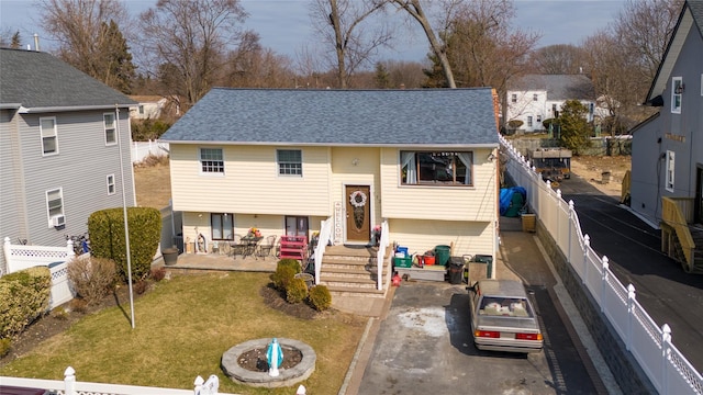 bi-level home featuring driveway, a shingled roof, an outdoor fire pit, and a fenced backyard