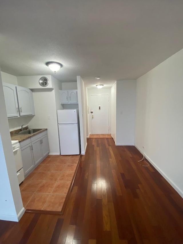 kitchen with freestanding refrigerator, wood-type flooring, a sink, and baseboards