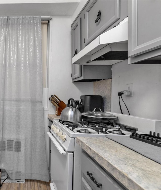 kitchen with wood finished floors, white gas stove, gray cabinetry, light countertops, and under cabinet range hood