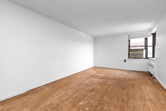 empty room featuring hardwood / wood-style flooring, radiator, cooling unit, and baseboards