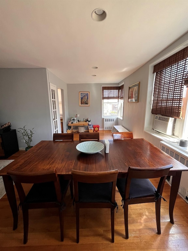 dining room with wood finished floors, radiator heating unit, a wall unit AC, and cooling unit