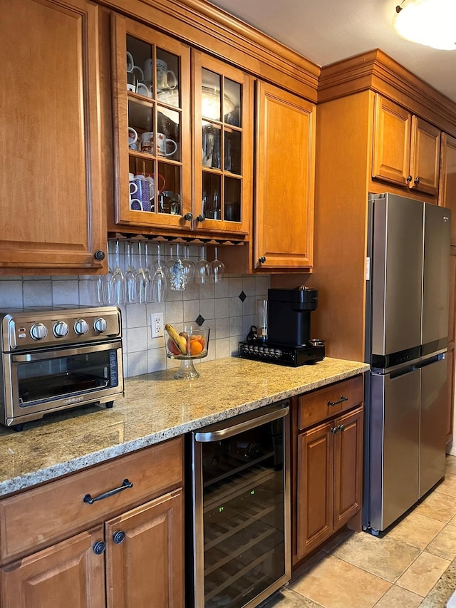 kitchen featuring tasteful backsplash, beverage cooler, brown cabinetry, and freestanding refrigerator