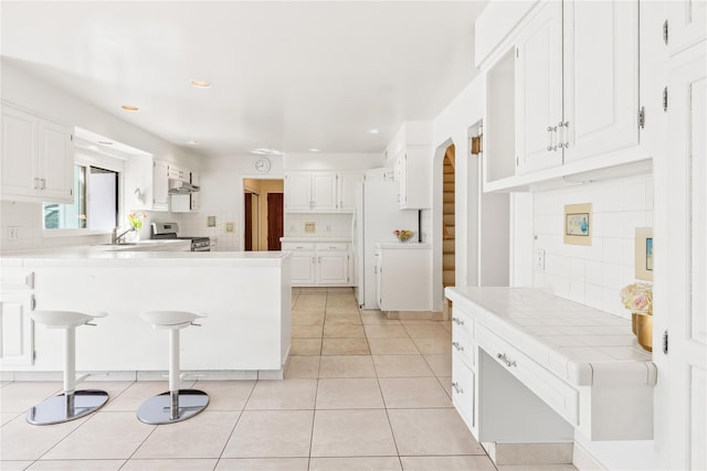 kitchen with light tile patterned floors, decorative backsplash, tile countertops, a peninsula, and stainless steel gas range