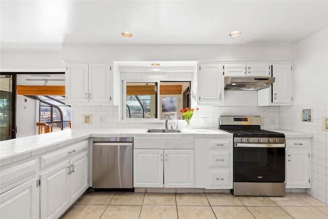 kitchen featuring stainless steel appliances, tile counters, a sink, and under cabinet range hood