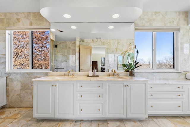 full bathroom featuring double vanity, tiled shower, a sink, and tile walls