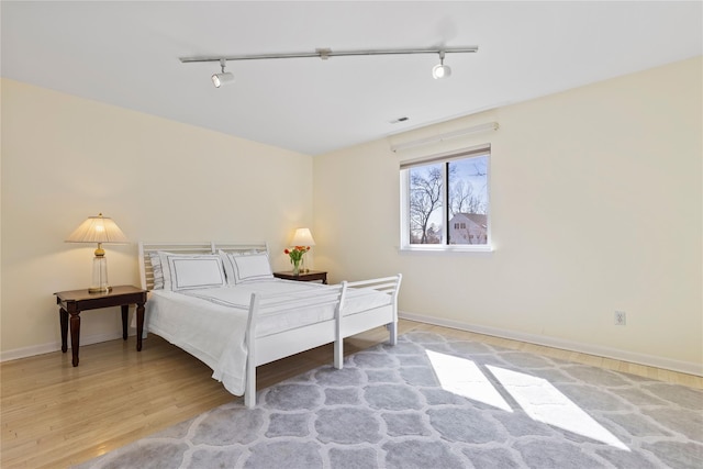 bedroom with baseboards, track lighting, visible vents, and wood finished floors