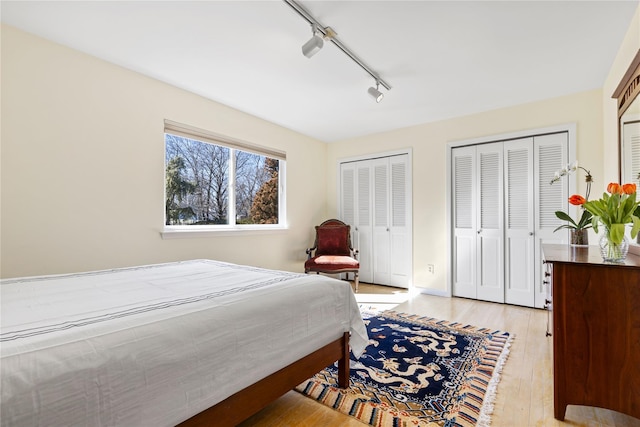 bedroom featuring light wood-style floors, track lighting, and multiple closets