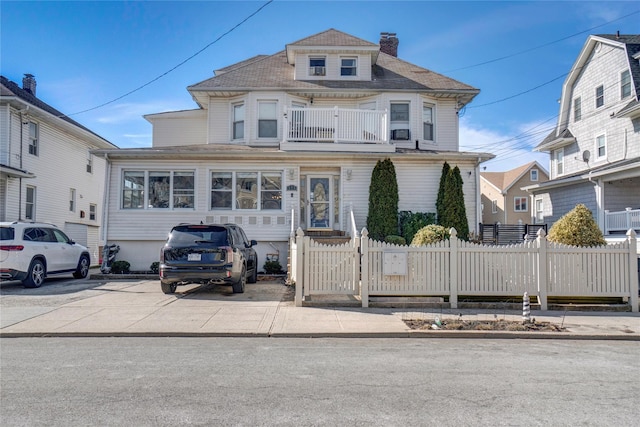 view of front of home featuring a fenced front yard, a chimney, and a balcony