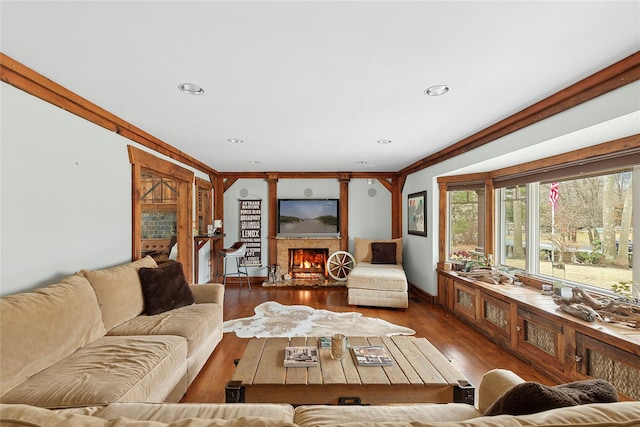 living room featuring a warm lit fireplace, dark wood-style floors, crown molding, and recessed lighting