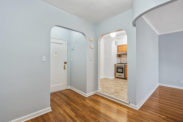 hallway featuring arched walkways, wood finished floors, and baseboards