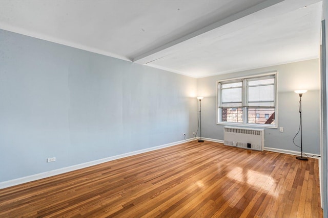 empty room with baseboards, hardwood / wood-style floors, and radiator heating unit