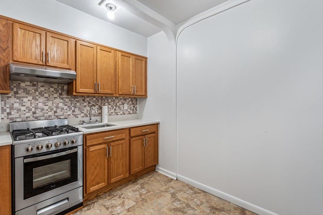 kitchen featuring light countertops, decorative backsplash, gas stove, a sink, and under cabinet range hood