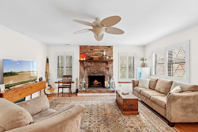 living room featuring visible vents, a ceiling fan, wood finished floors, crown molding, and a brick fireplace