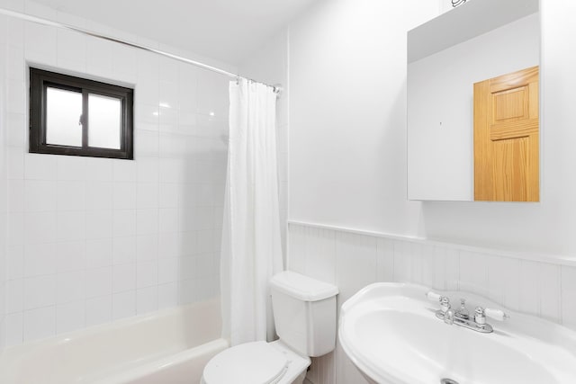 full bath featuring toilet, a wainscoted wall, a sink, and shower / tub combo with curtain