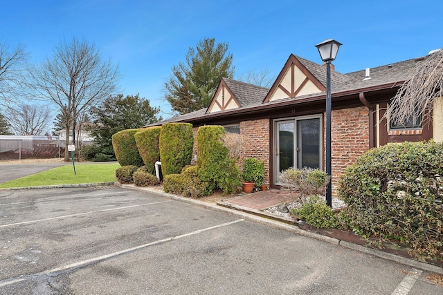 exterior space with brick siding, a shingled roof, a yard, stucco siding, and uncovered parking