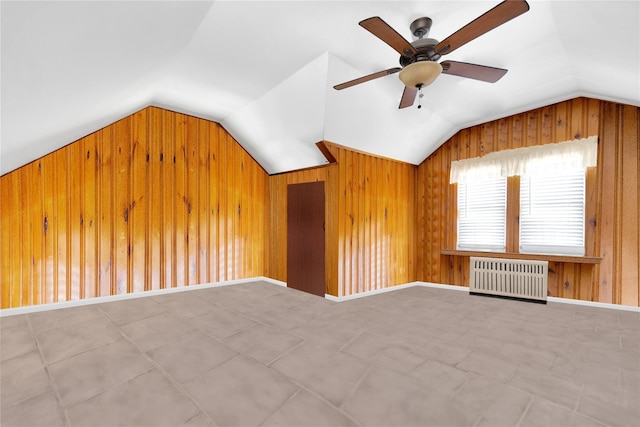 additional living space with lofted ceiling, wooden walls, a ceiling fan, baseboards, and radiator heating unit