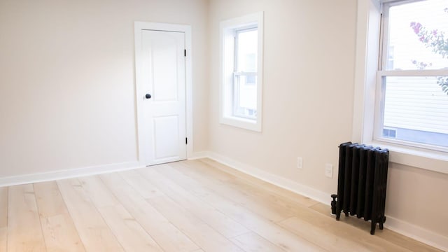 empty room featuring radiator, light wood finished floors, and baseboards