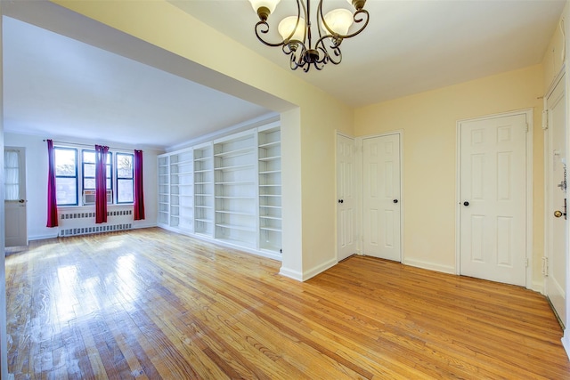 empty room featuring built in shelves, a notable chandelier, radiator, light wood-style flooring, and baseboards