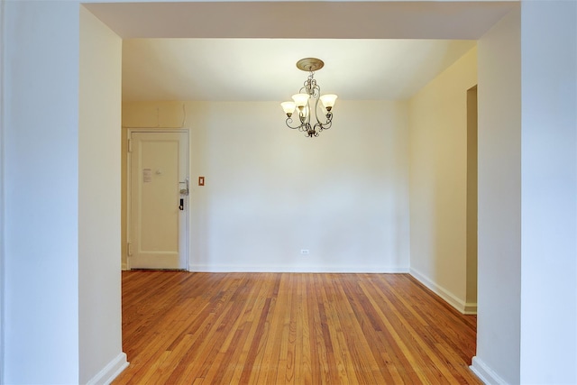 unfurnished room featuring baseboards, light wood finished floors, and an inviting chandelier