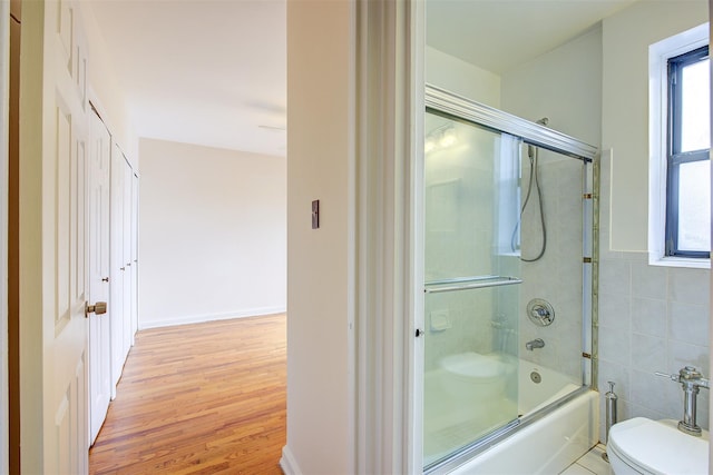 bathroom with combined bath / shower with glass door, tile walls, toilet, and wood finished floors