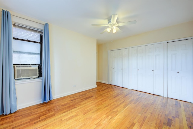 unfurnished bedroom with ceiling fan, cooling unit, baseboards, light wood-style floors, and two closets