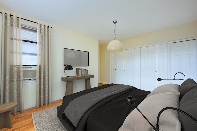 bedroom with wood finished floors, two closets, and baseboards