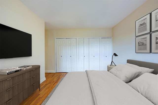 bedroom with multiple closets, light wood-style flooring, and baseboards