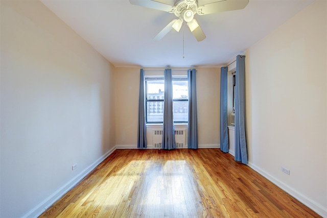 empty room with a ceiling fan, radiator, baseboards, and wood finished floors