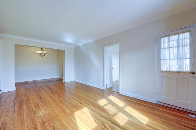 unfurnished living room featuring a chandelier, light wood-type flooring, and baseboards