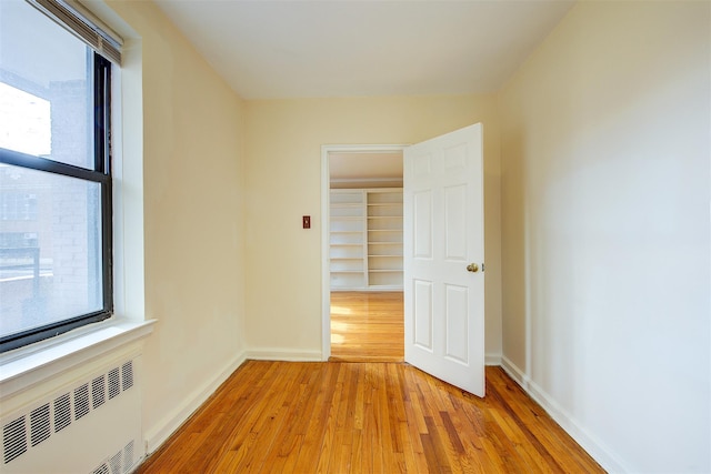 unfurnished room with baseboards, light wood finished floors, and radiator