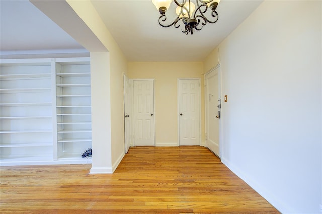 hall featuring light wood-style floors, built in shelves, baseboards, and an inviting chandelier