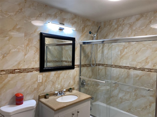 bathroom featuring shower / bath combination with glass door, vanity, toilet, and tile walls