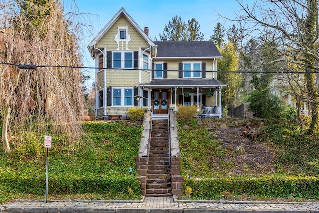 victorian home with covered porch, a chimney, and french doors