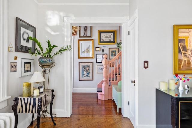 hallway with stairs, ornamental molding, wood finished floors, and baseboards