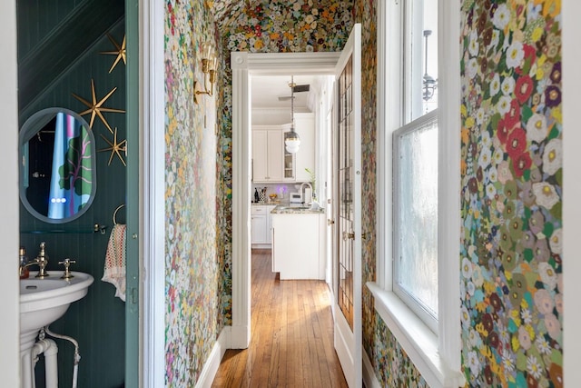 bathroom featuring wood finished floors, a sink, backsplash, and wallpapered walls