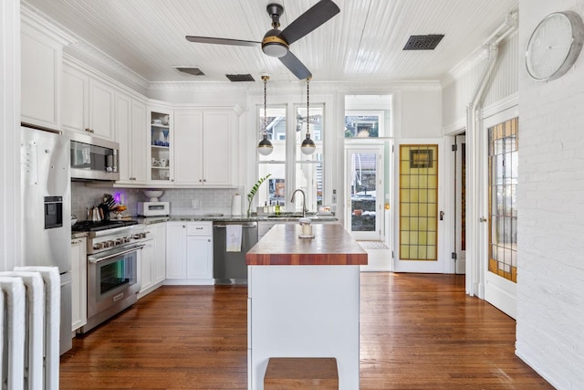 kitchen with appliances with stainless steel finishes, glass insert cabinets, butcher block counters, and dark wood finished floors